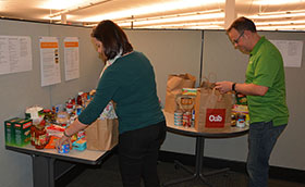 Two VAA employees at some tables filled with food items to donate