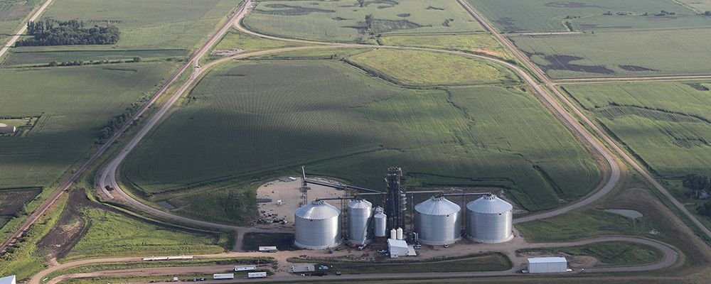 Wide exterior shot from high overhead of a steel agricultural facility with a rural backdrop