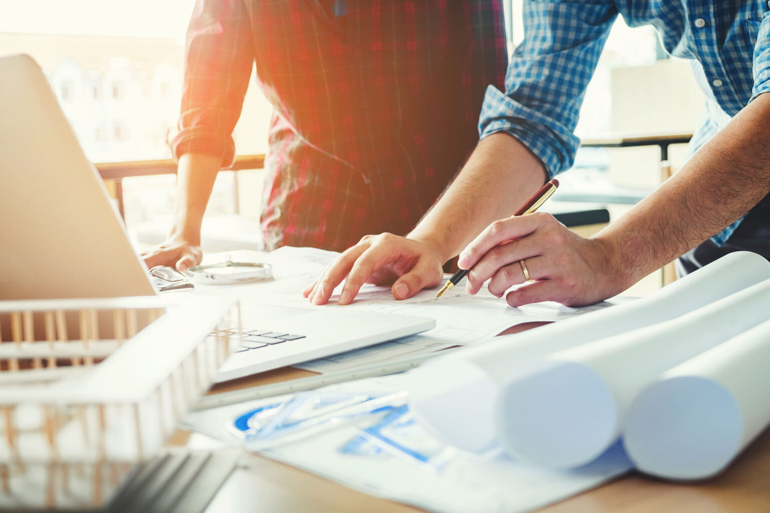 Stock photo of two colleagues' hands on a desktop with one of them drawing on a blueprint