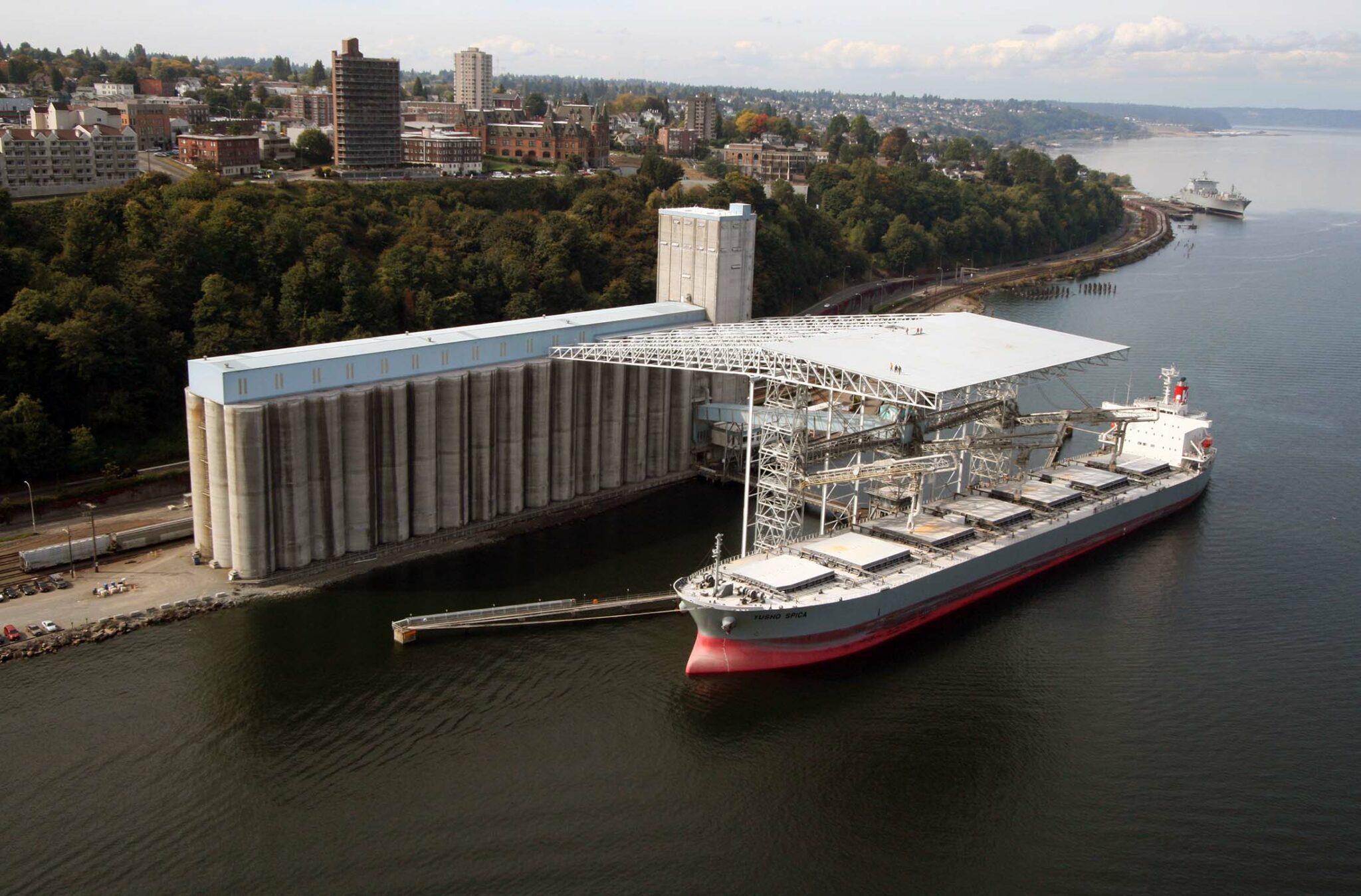 Wide exterior shot of a large ship at a port with a city in the background