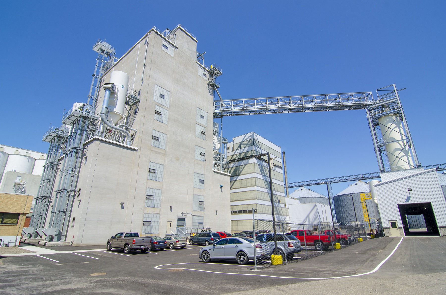 Exterior view of large grain cleaning facility with vehicles parked in the foreground