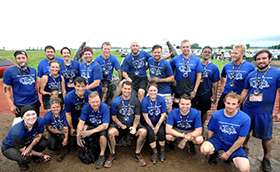 A group in matching t-shirts gathers on a muddy course for a photo