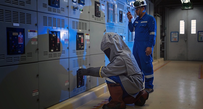 Two safety workers access an electrical panel