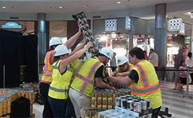 A group of employees in safety gear construct a can display