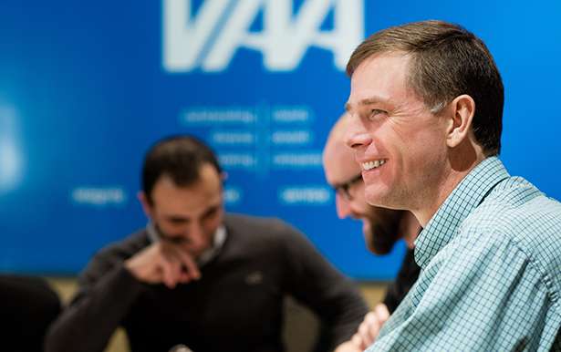 Candid photo of a man in a dress shirt smiling at a conference table with his colleagues