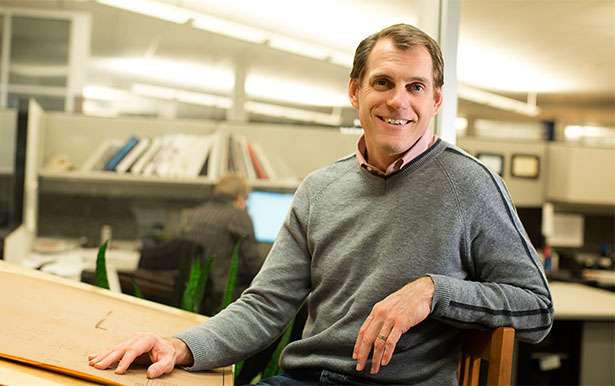 Profile photo of a man in a gray sweater smiling from a drafting table