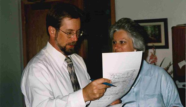 Candid photo of a man in glasses and white dress shirt speaking to a woman while holding a sheet of paper