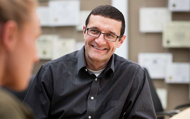 Candid photo of a man in glasses and dress shirt smiling at another colleague