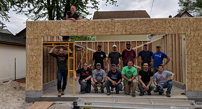 A group of volunteers pose and smile at a new house construction site