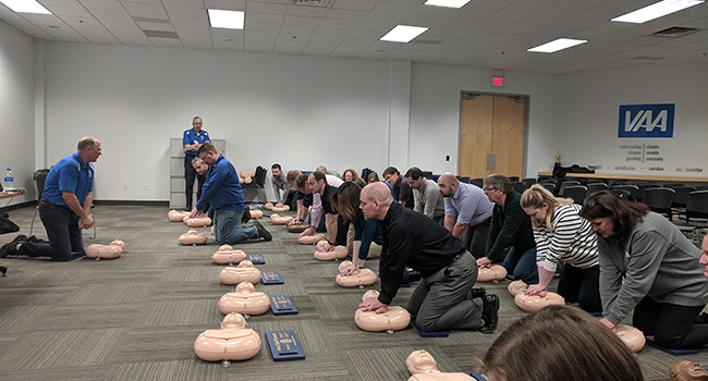 A group of employees gather at a CPR class with practice dummies