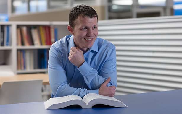 Profile photo of a young man in a blue dress shirt with a book opened in front of him