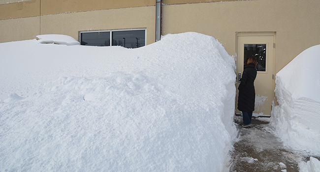 A woman accesses a door next to a large snow drift