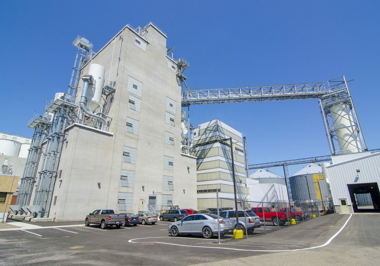 Exterior view of large grain cleaning facility with vehicles parked in the foreground